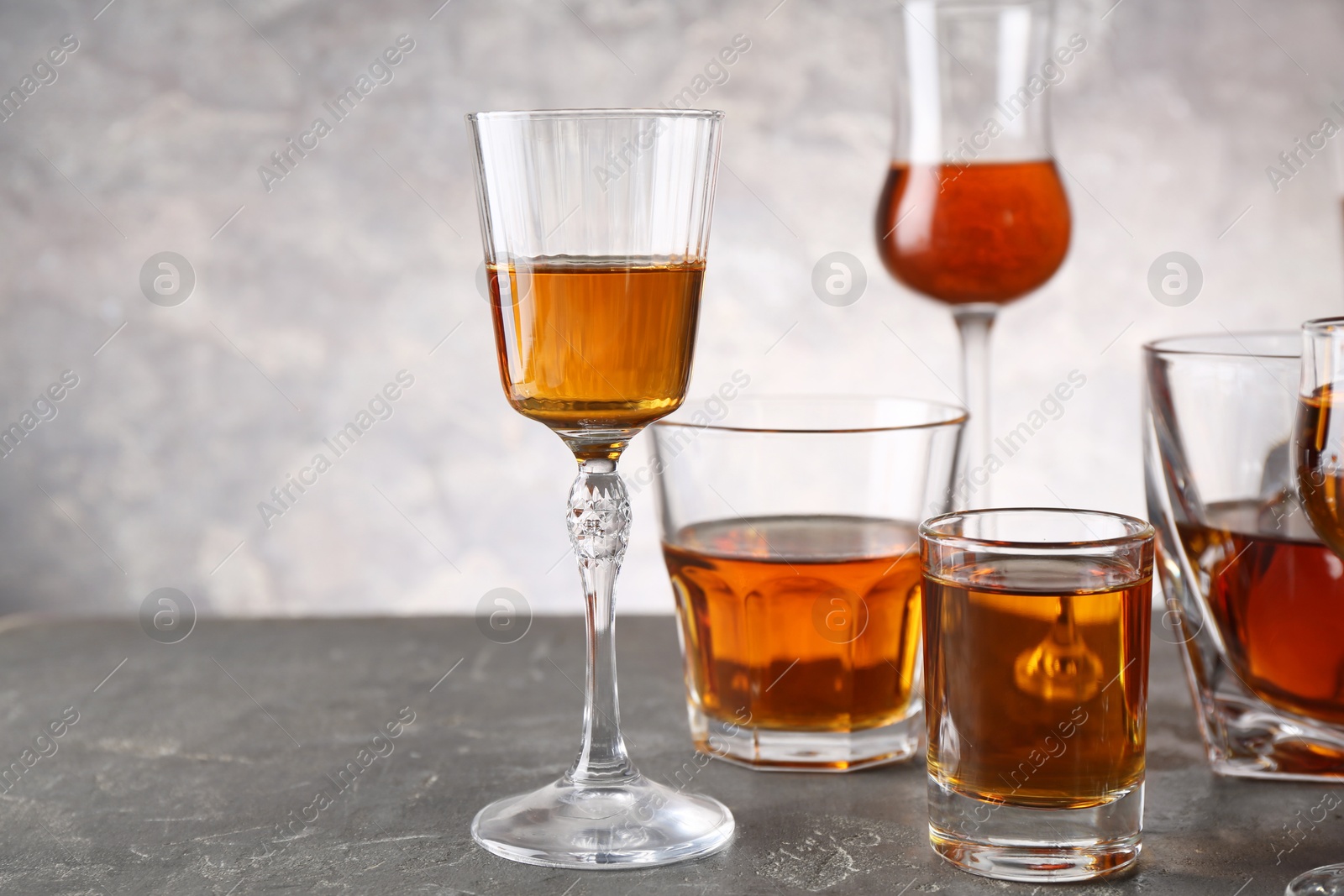 Photo of Different delicious liqueurs in glasses on grey table, space for text