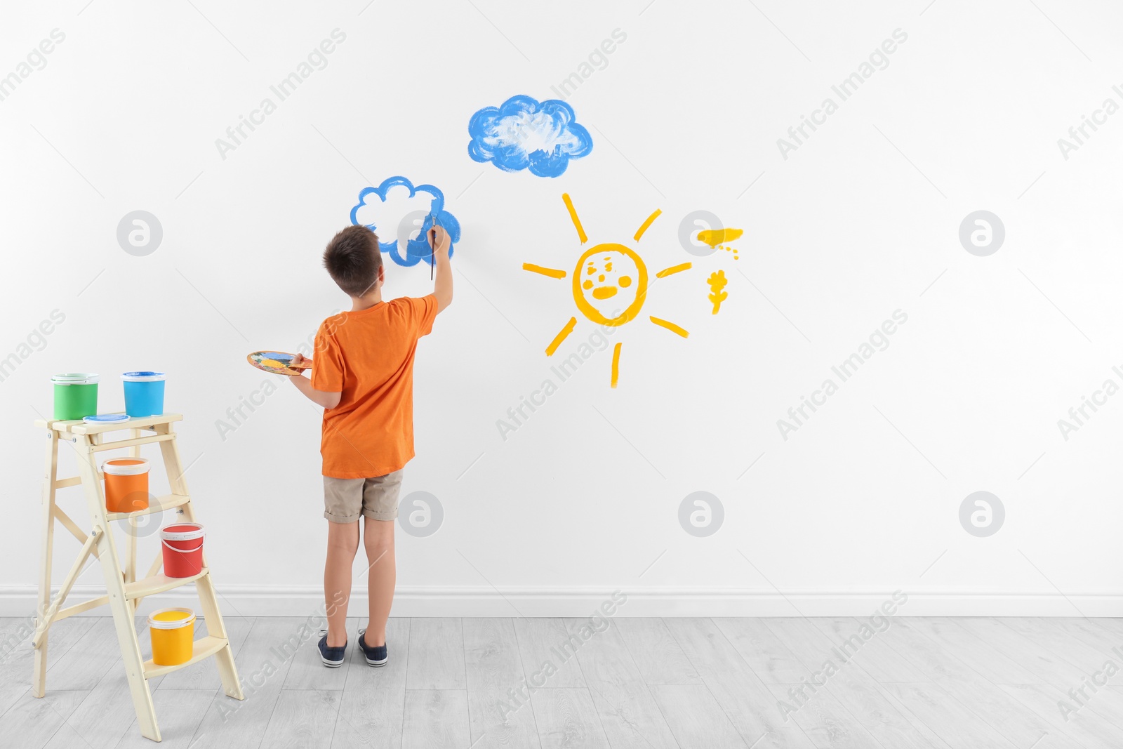 Photo of Little child painting cloud on white wall in room