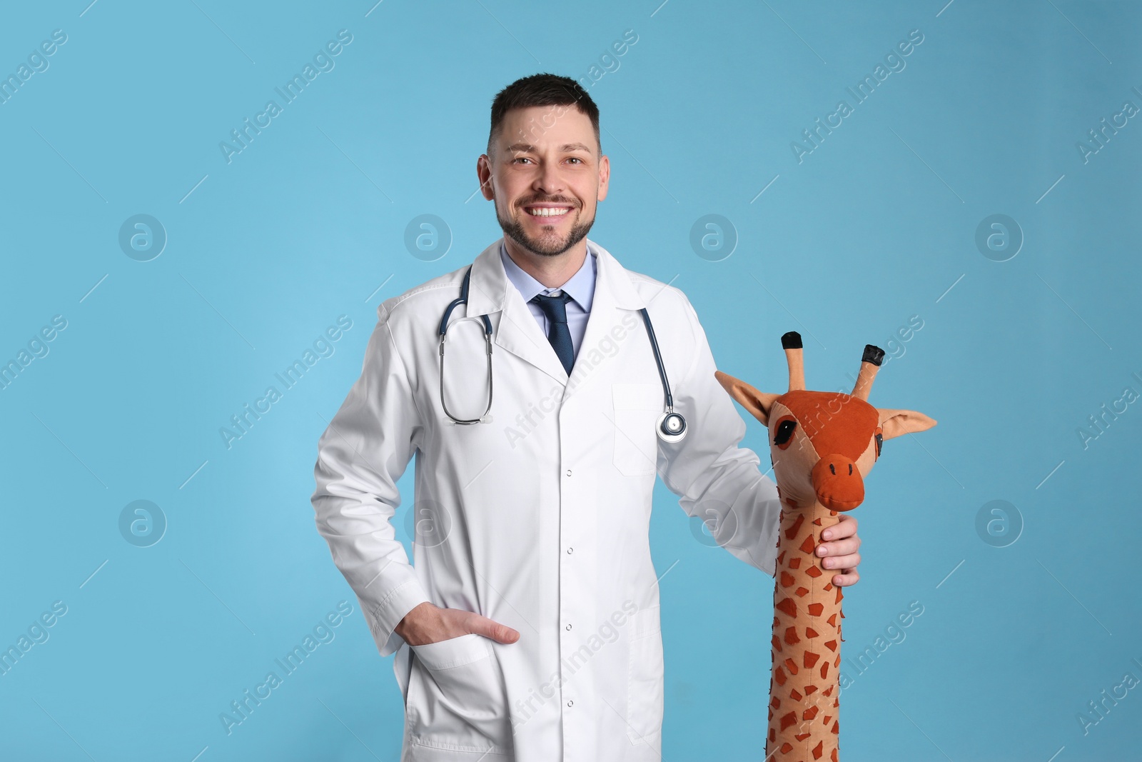 Photo of Pediatrician with toy giraffe and stethoscope on light blue background