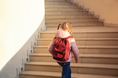 Photo of Cute little girl with backpack on stairs outdoors, back view