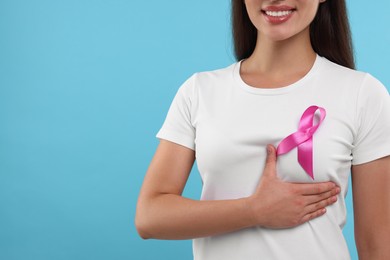 Photo of Woman with pink ribbon on light blue background, closeup and space for text. Breast cancer awareness