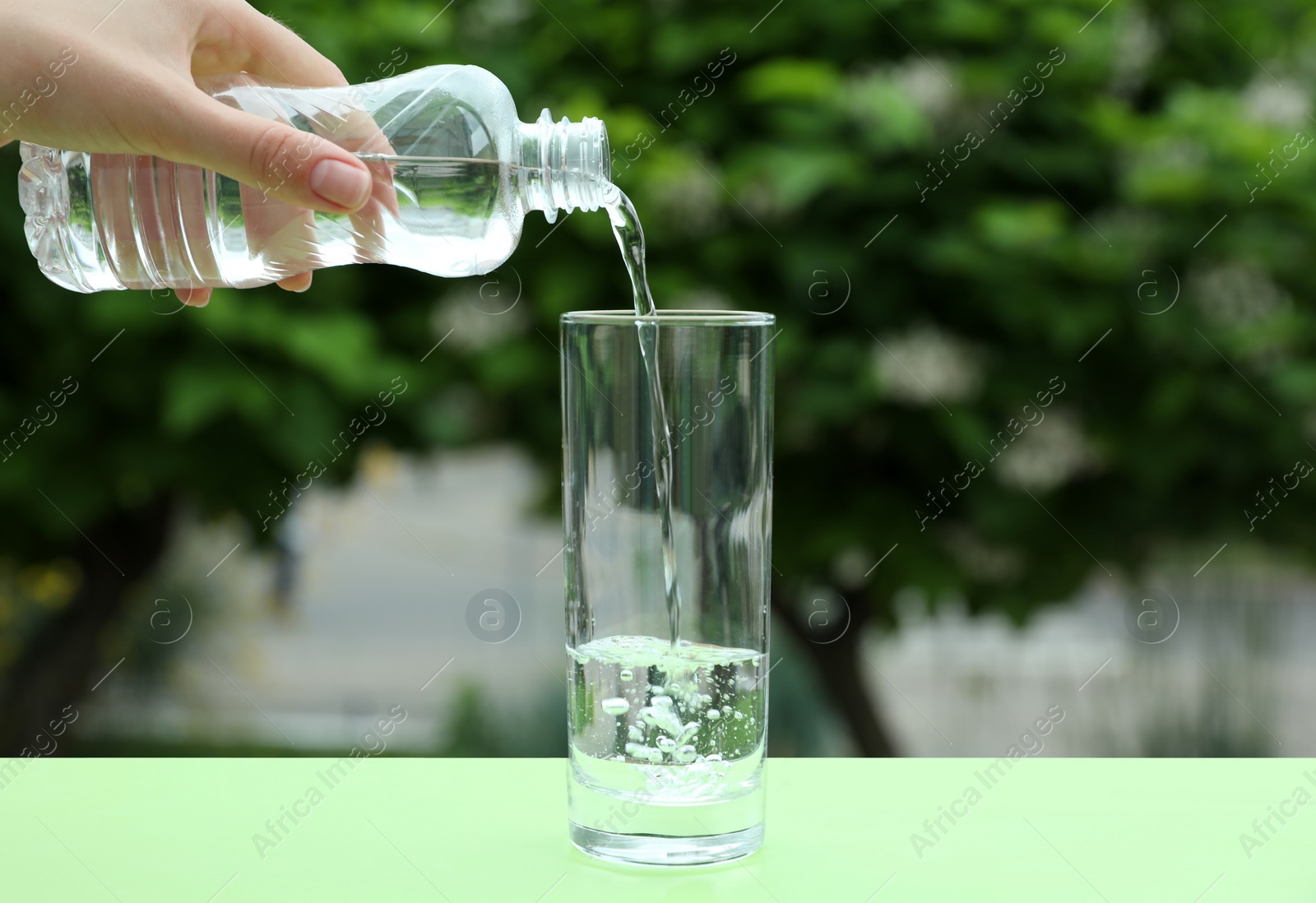 Photo of Woman pouring water from bottle into glass on table outdoors, closeup