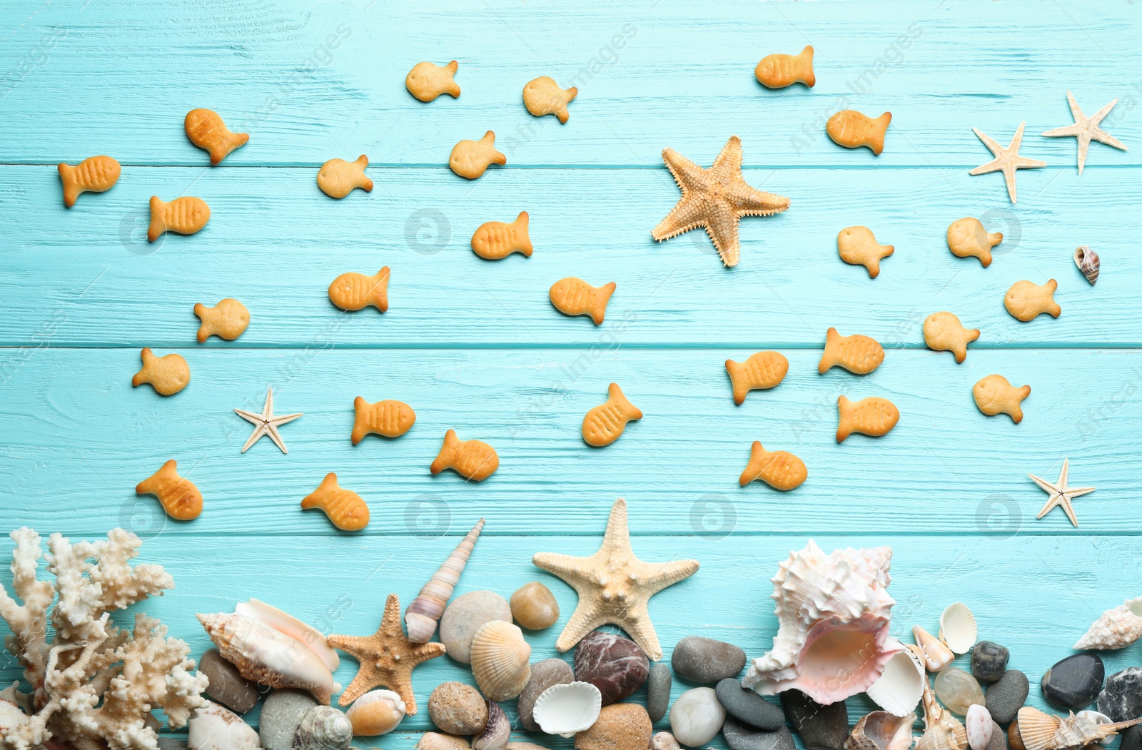 Photo of Underwater life represented with goldfish crackers on light blue wooden table, flat lay