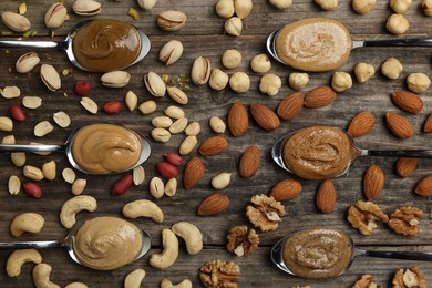 Photo of Tasty nut butters in spoons and raw nuts on wooden table, flat lay