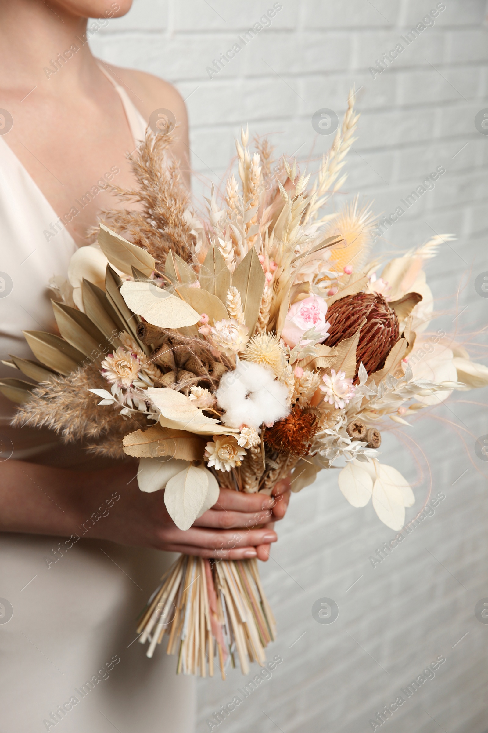 Photo of Bride holding beautiful dried flower bouquet near white brick wall, closeup