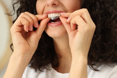 Photo of Young woman applying whitening strip on her teeth indoors, closeup