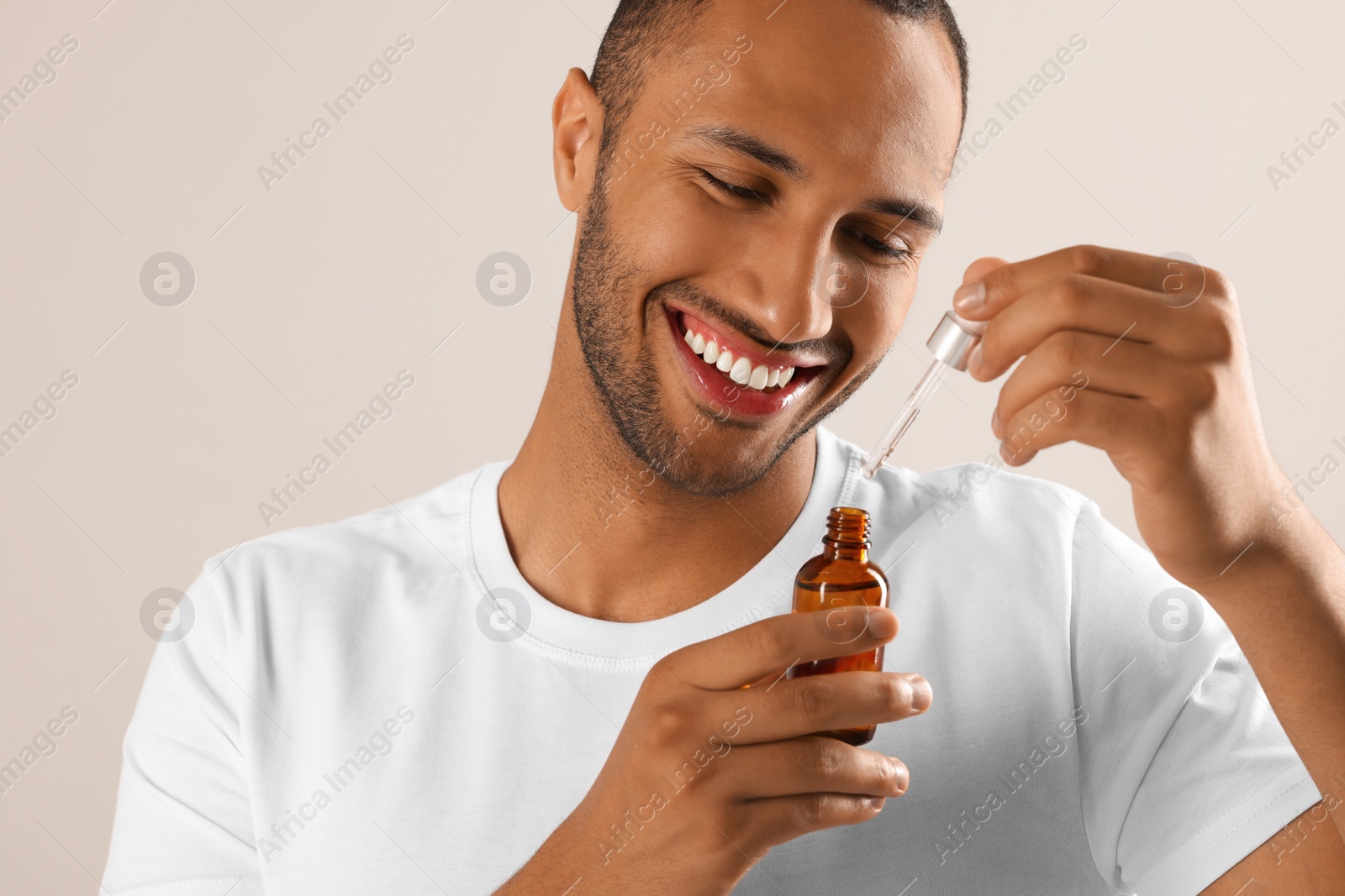 Photo of Handsome man with cosmetic serum in hands on light grey background