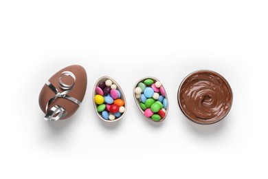 Photo of Delicious chocolate eggs, paste and colorful candies on white background, flat lay