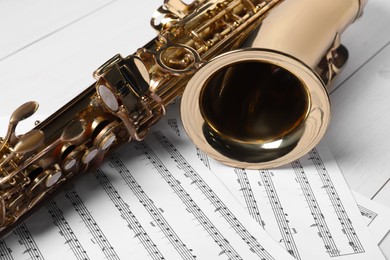 Photo of Beautiful saxophone and note sheets on white wooden background, closeup