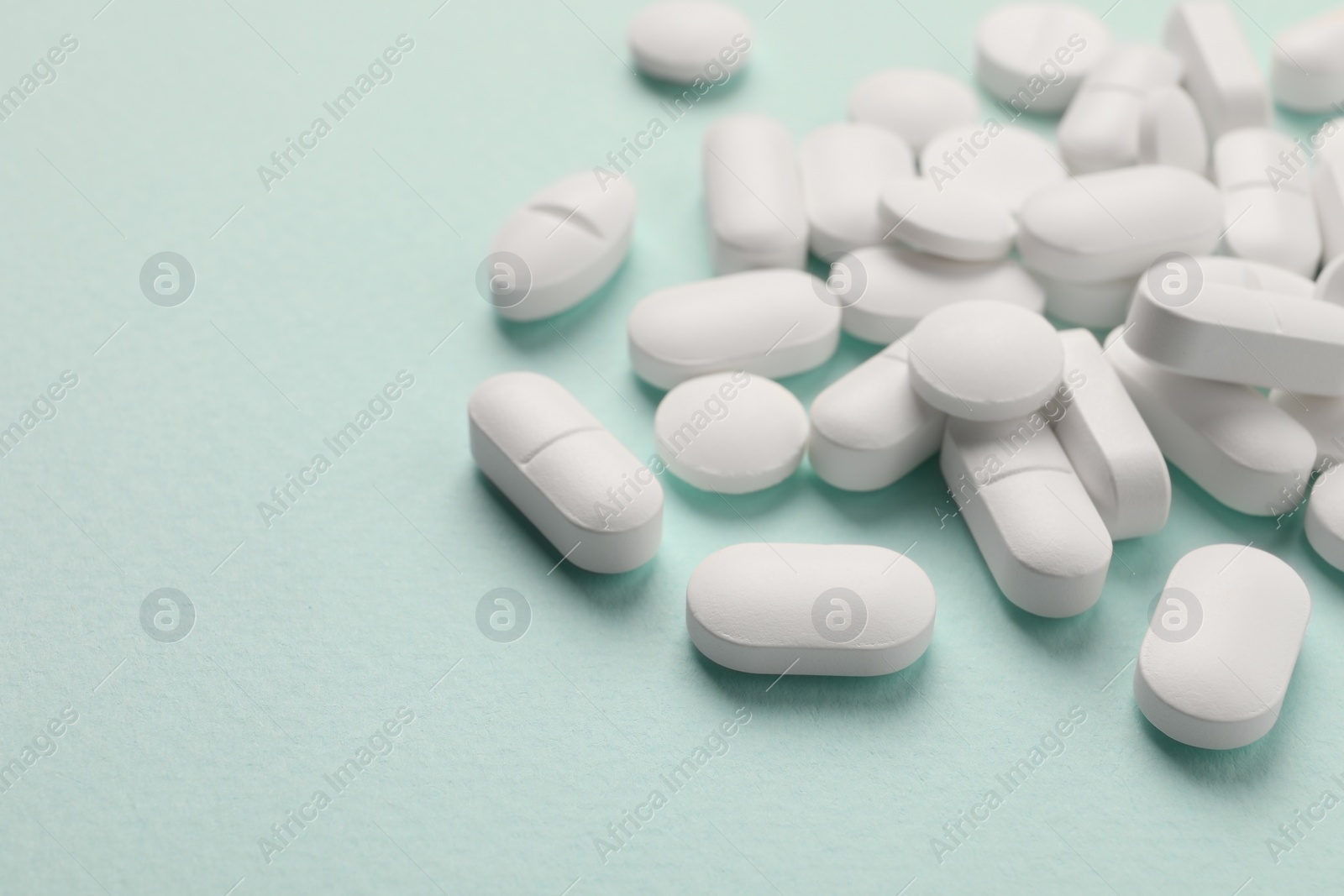 Photo of Pile of white pills on mint background, selective focus. Space for text