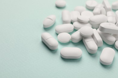 Pile of white pills on mint background, selective focus. Space for text