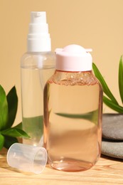 Bottles of micellar water, green leaves and spa stones on wooden table against beige background, closeup