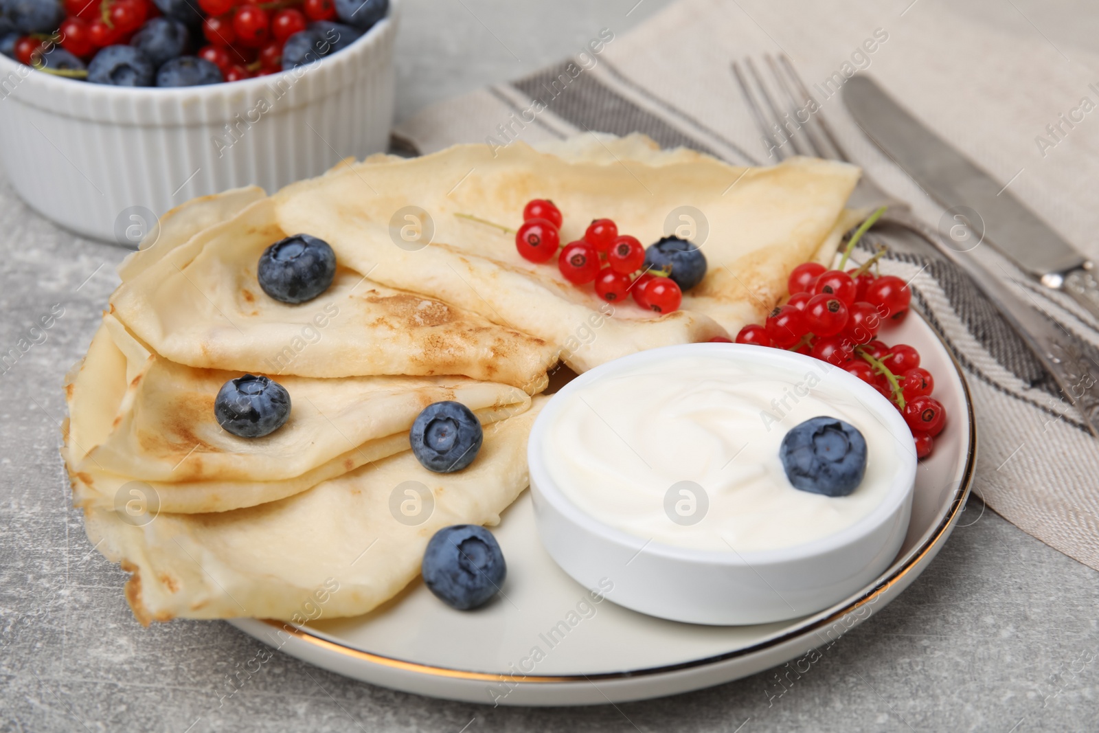 Photo of Delicious crepes with natural yogurt, blueberries and red currants on grey table