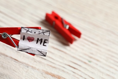 Photo of Open red clothespin and piece of paper with handwritten phrase I Love Me over white table, closeup. Space for text