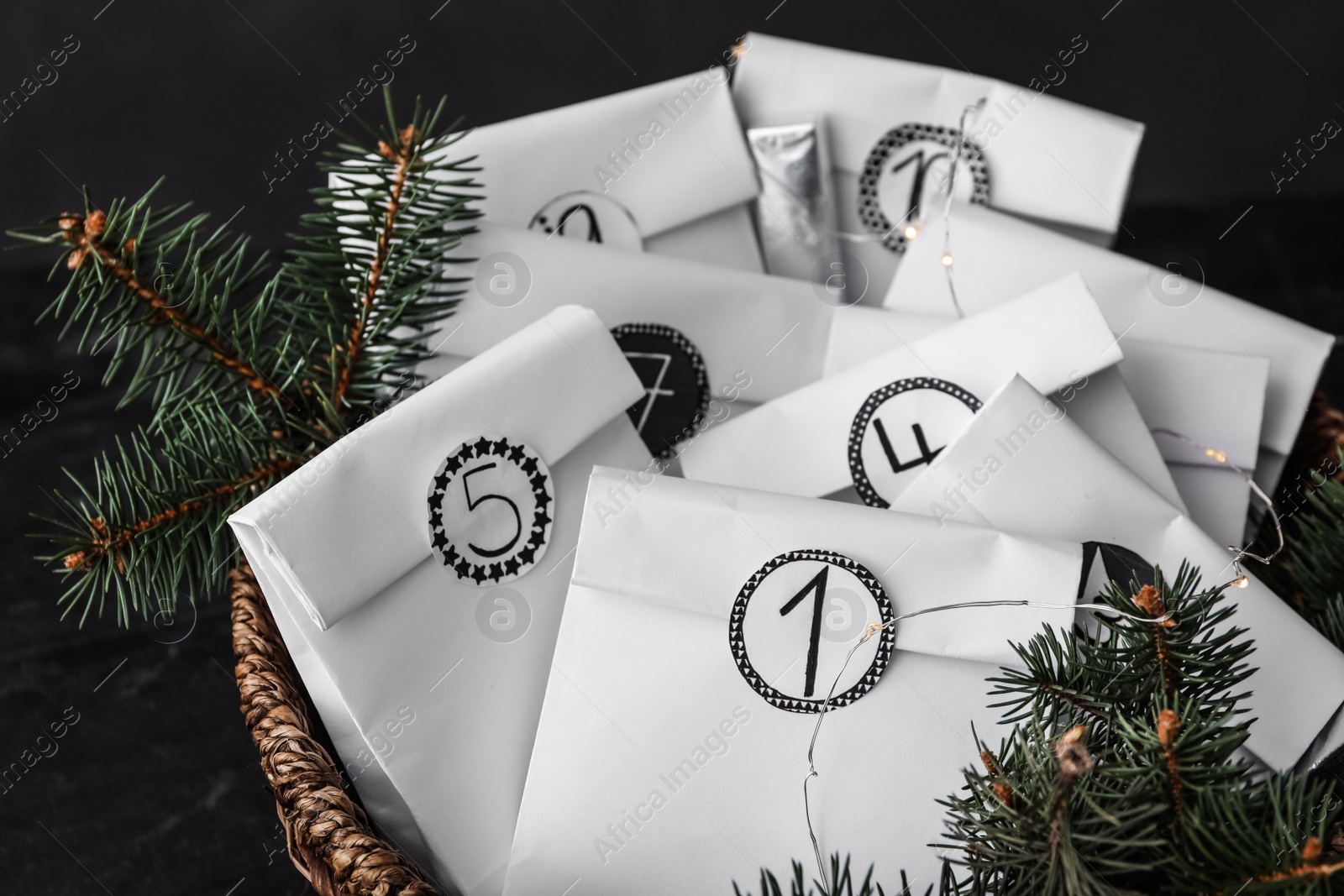 Photo of Paper bags, fir branches and garland in wicker basket, closeup. Christmas advent calendar