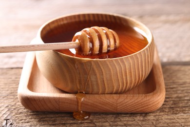 Photo of Delicious honey in bowl and dipper on wooden table, closeup