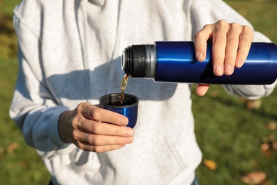 Photo of Woman pouring hot drink from thermos into cap outdoors, closeup