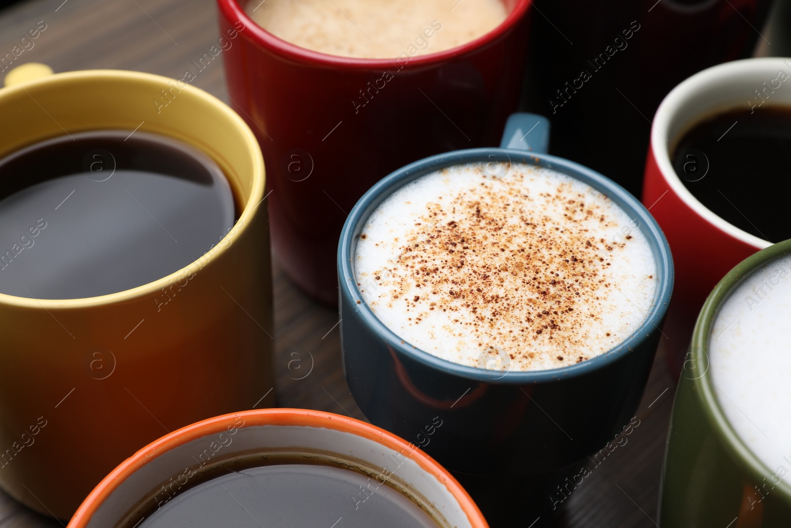 Photo of Many different cups with aromatic hot coffee on wooden table, closeup