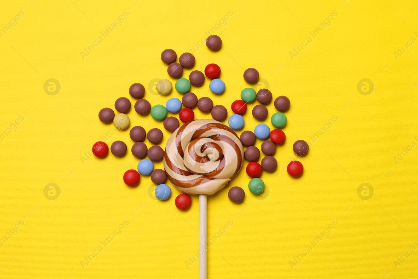 Photo of Delicious lollipop and candies on yellow background, flat lay