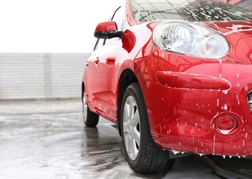 Photo of Red auto with foam at car wash. Space for text