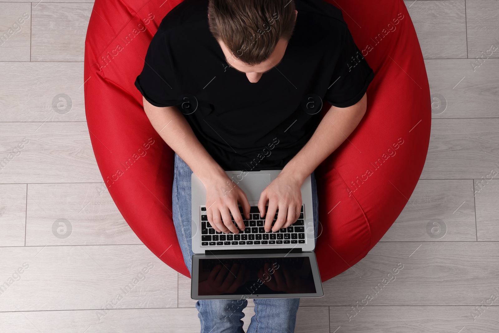 Photo of Man working with laptop in beanbag chair, top view