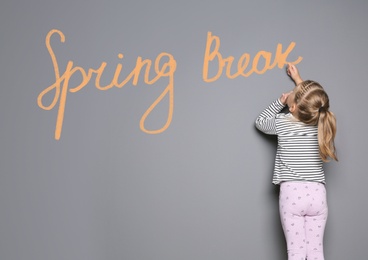 Image of Small girl writing phrase Spring Break with chalk on grey wall. School holiday