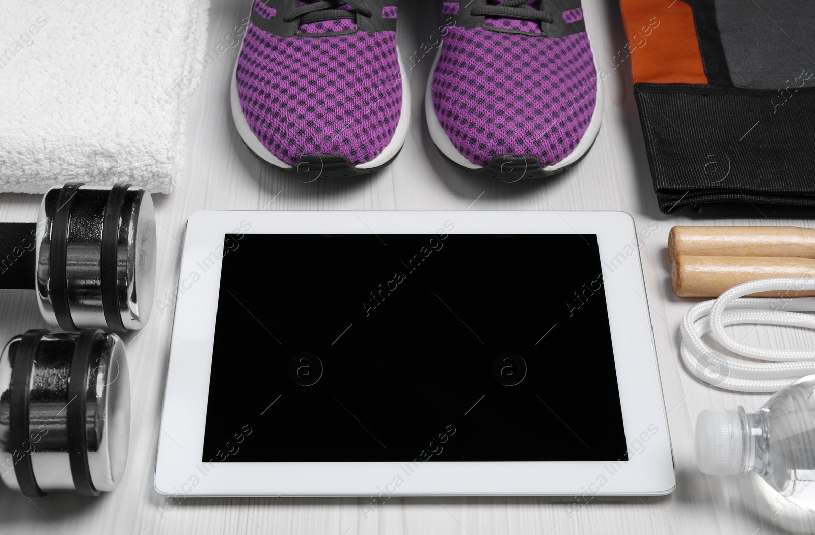 Photo of Tablet, clothes and sports equipment on white wooden table. Personal training