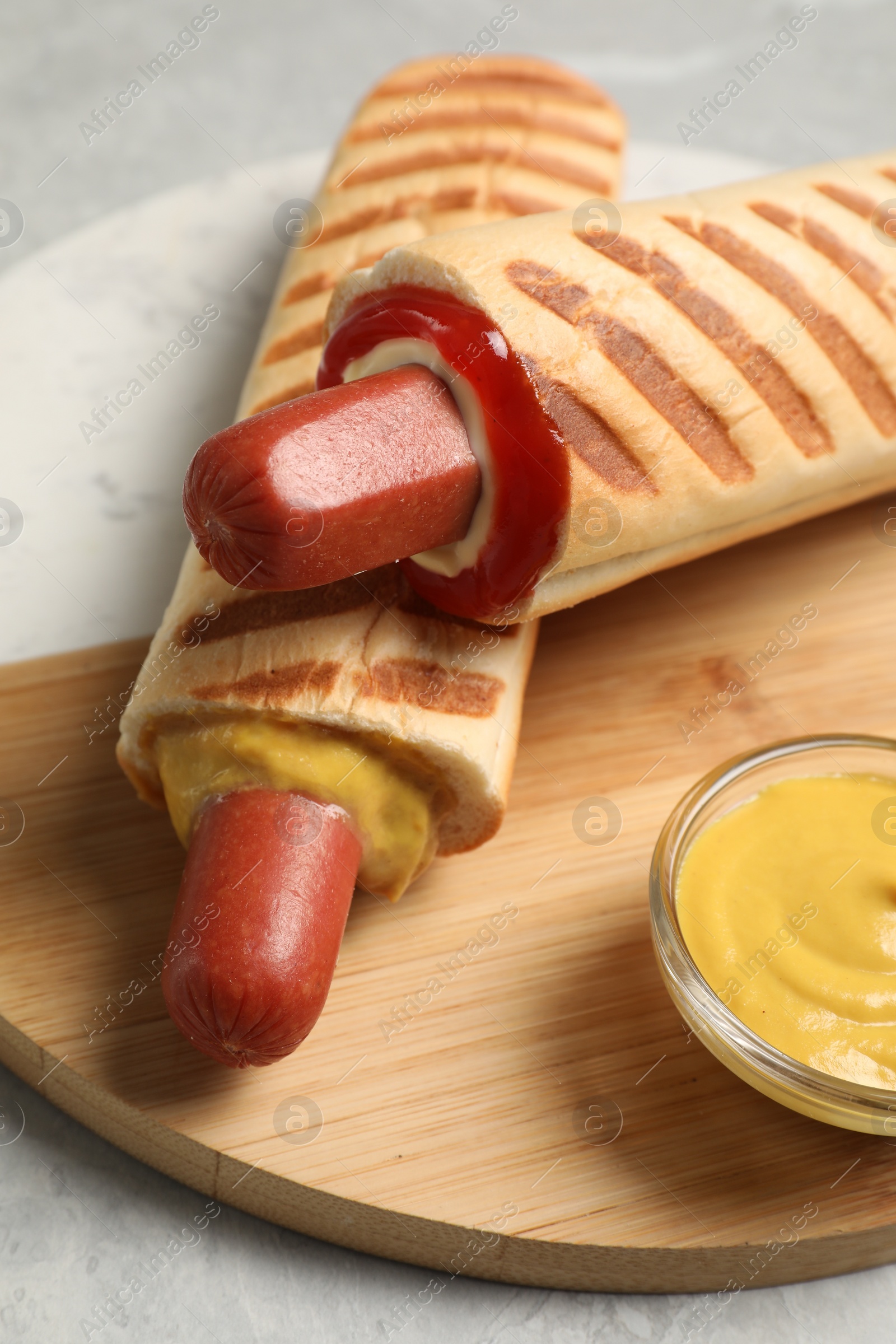 Photo of Tasty french hot dogs and dip sauce on serving board, closeup