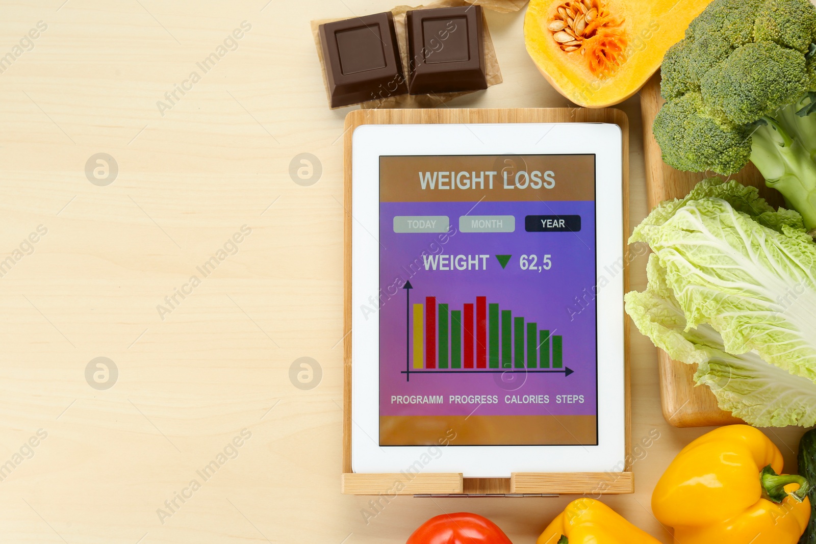 Photo of Tablet with weight loss calculator application and food products on wooden table, flat lay. Space for text