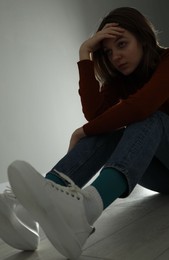 Photo of Sad young woman sitting on floor near grey wall indoors