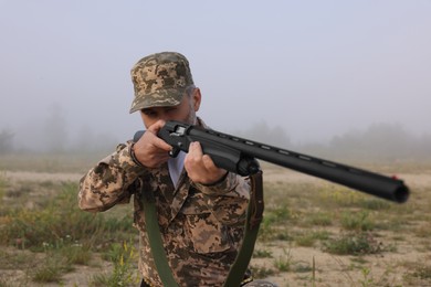 Photo of Man wearing camouflage and aiming with hunting rifle outdoors