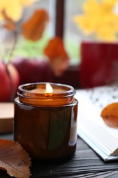 Photo of Beautiful burning candle and book on wooden table near window. Autumn atmosphere