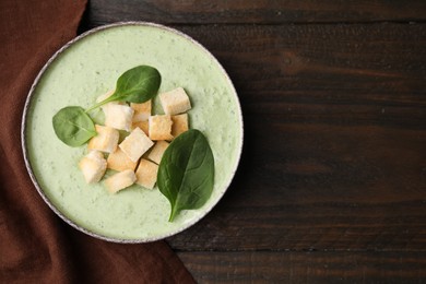 Photo of Delicious spinach cream soup with leaves and croutons in bowl on wooden table, top view. Space for text