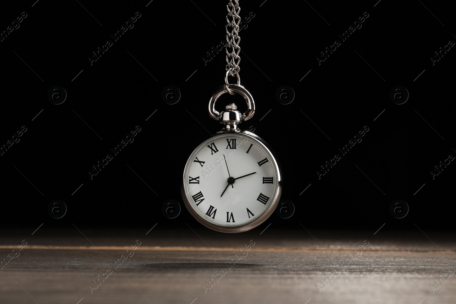 Photo of Beautiful vintage pocket watch with silver chain on black background above wooden table. Hypnosis session