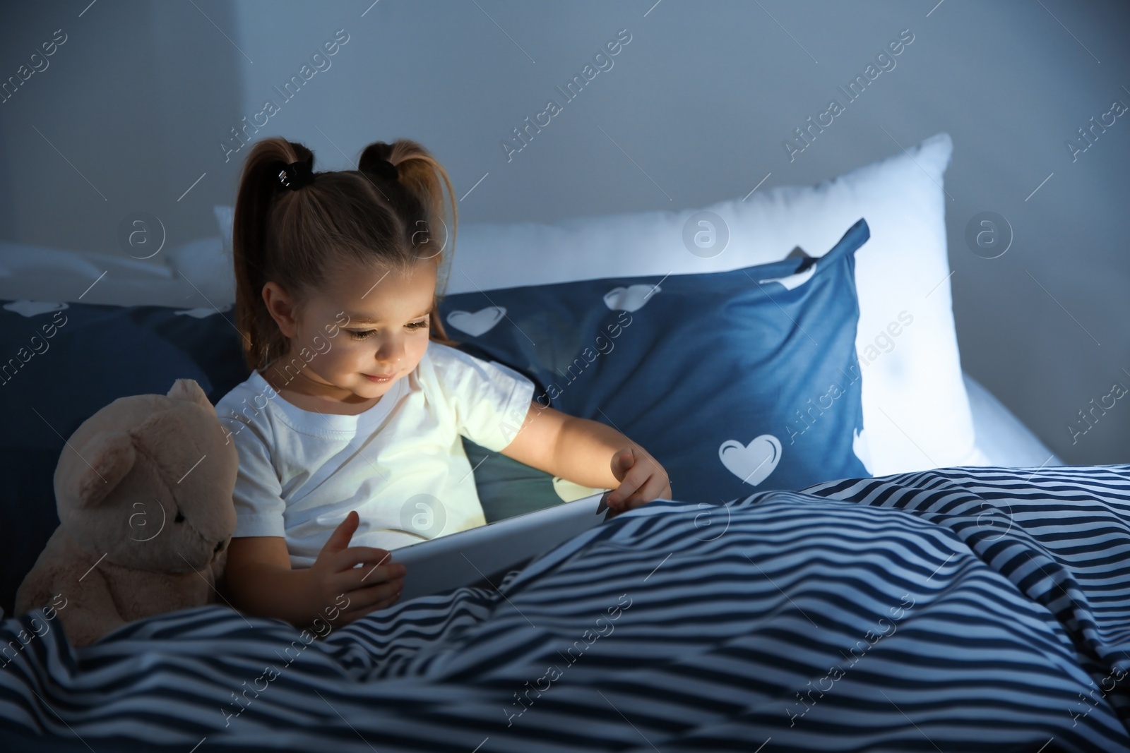 Photo of Beautiful little girl with gadget and toy in bed at night. Bedtime schedule