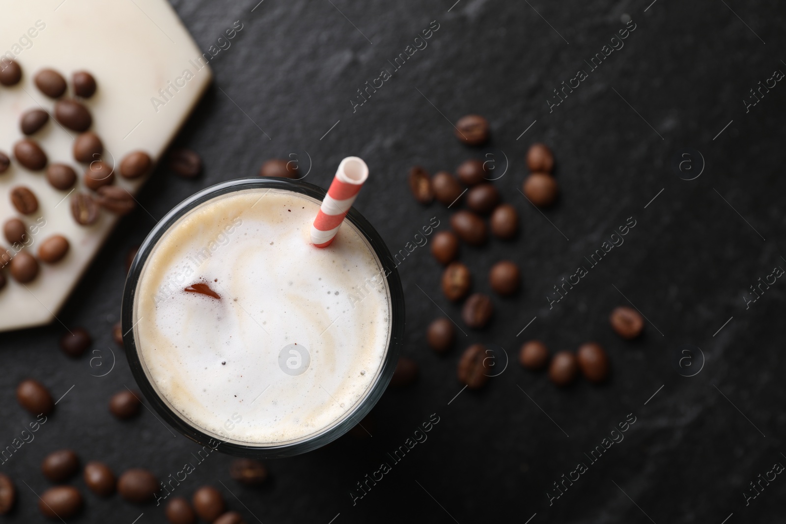 Photo of Refreshing iced coffee with milk in glass and beans on dark gray table, top view