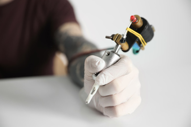 Photo of Tattoo artist with professional machine at table against light background, closeup