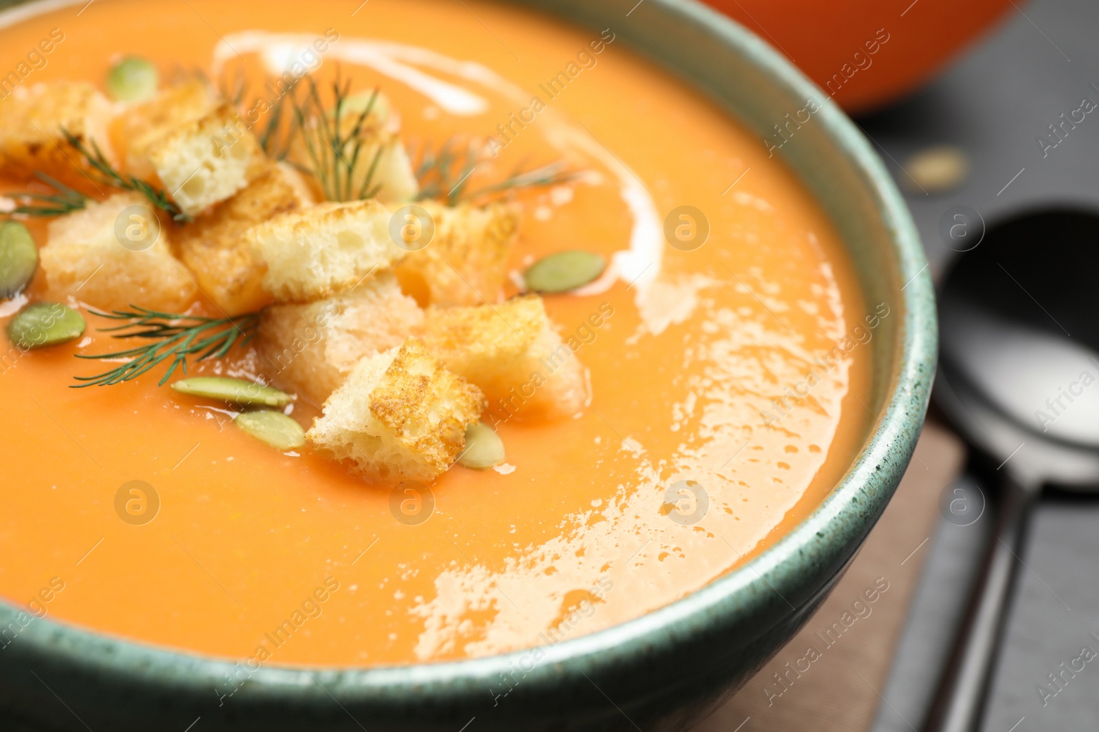 Photo of Delicious pumpkin soup in bowl served on black table, closeup