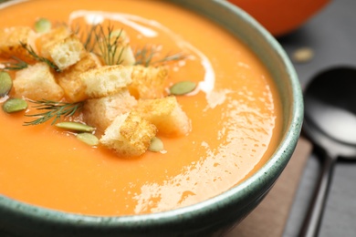 Photo of Delicious pumpkin soup in bowl served on black table, closeup