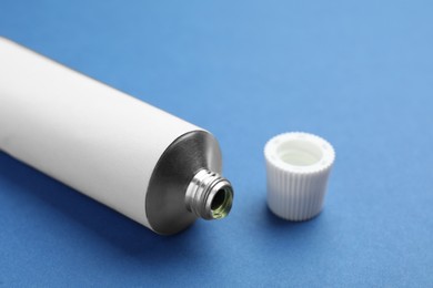 Photo of Open white tube of ointment on blue background, closeup
