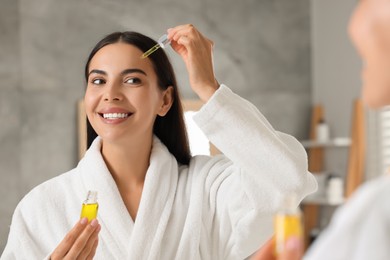 Photo of Beautiful young woman applying serum onto her face in bathroom