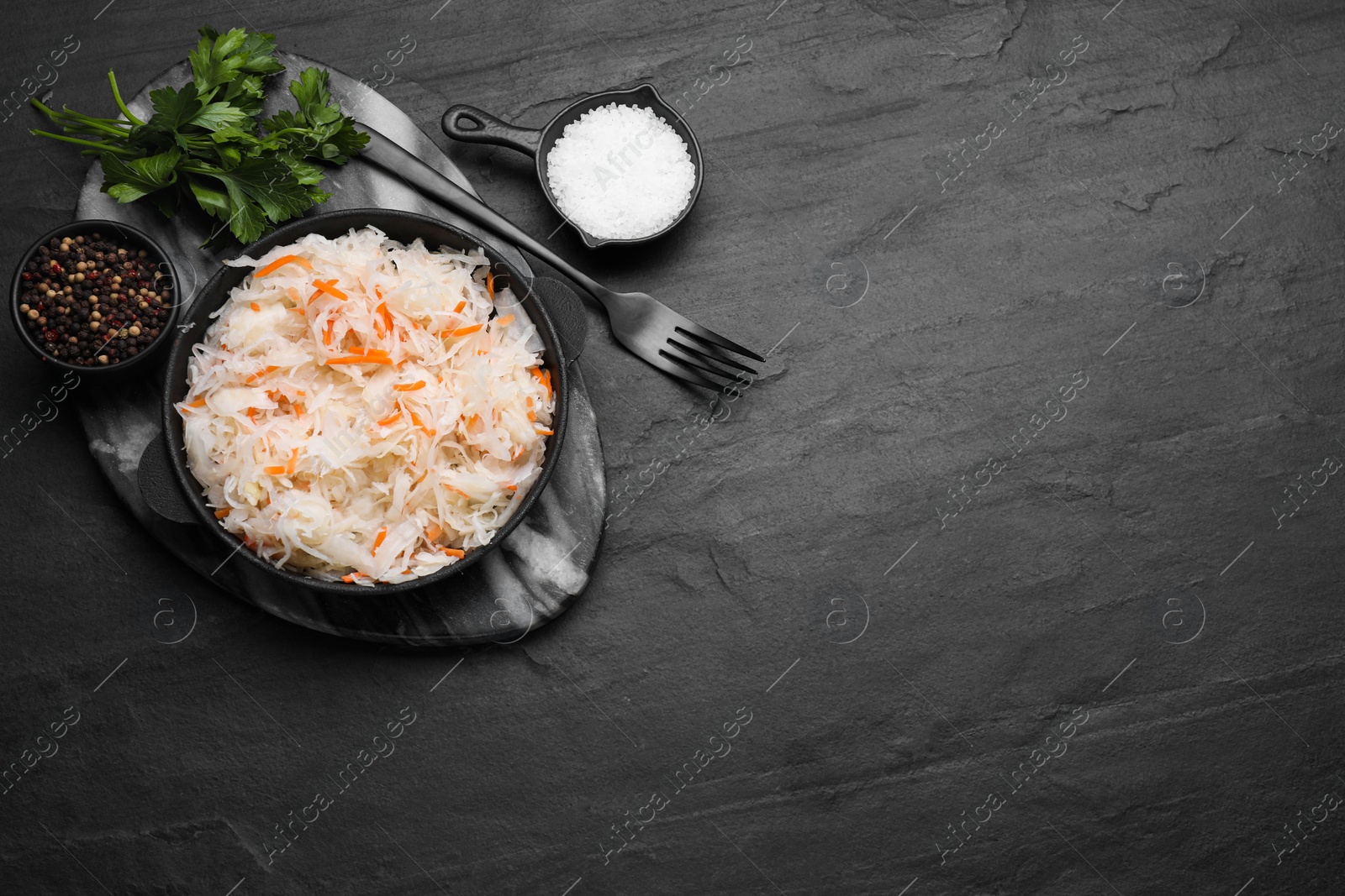 Photo of Bowl of tasty sauerkraut and ingredients on black table, flat lay. Space for text