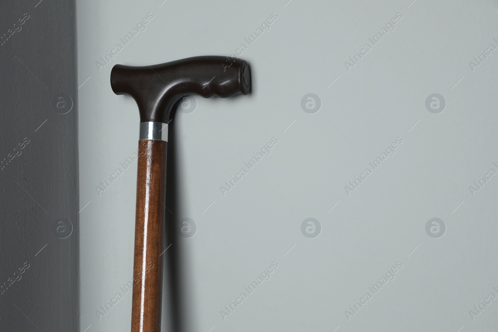 Photo of Elegant walking cane near light grey wall, closeup. Space for text