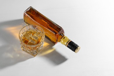 Photo of Whiskey with ice cubes in glass and bottle on white table, above view