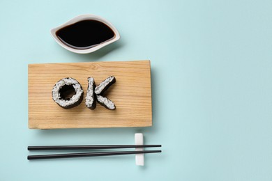 Word Ok made of sushi rolls, chopsticks and soy sauce on light turquoise background, flat lay. Space for text