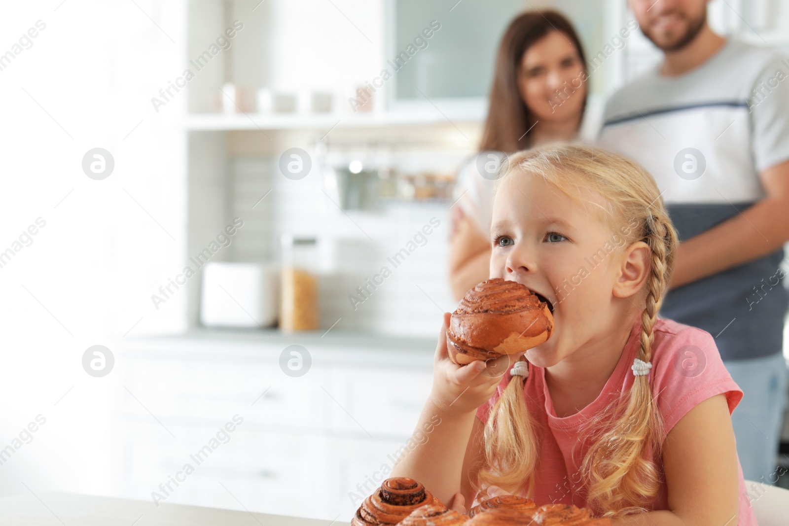 Photo of Little girl eating freshly oven baked bun in kitchen. Space for text