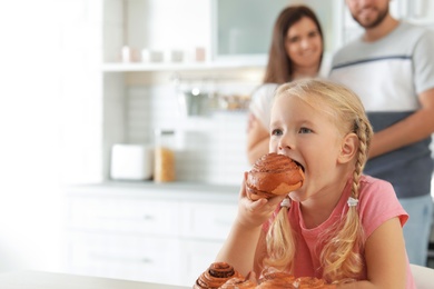 Photo of Little girl eating freshly oven baked bun in kitchen. Space for text