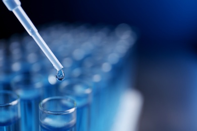 Dripping reagent into test tube with liquid sample on blurred background, closeup and space for text. Laboratory analysis