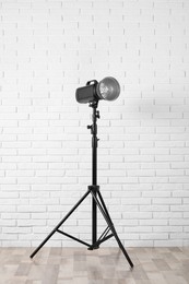 Photo of Professional studio flash light with reflector on tripod near white brick wall in room. Photography equipment