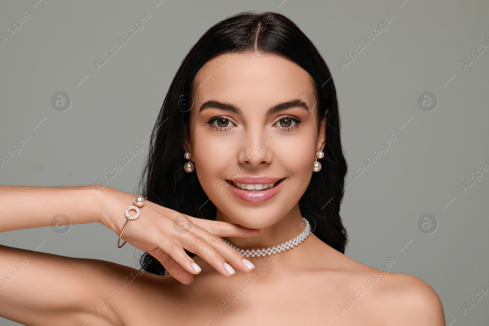Photo of Young woman wearing elegant pearl jewelry on grey background